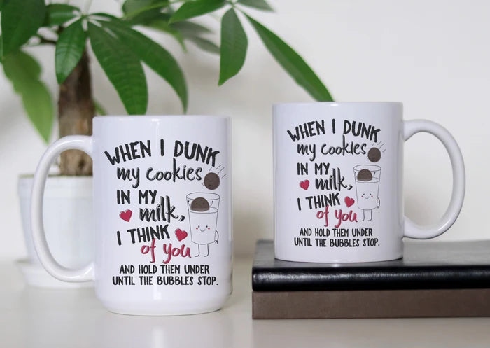 Dunking Delights white ceramic coffee mug featuring cute cookies, a smiling glass of milk, red hearts and the funny “When I dunk my cookies in my milk, I think of you” dark-humor design, available in 11 oz and 15 oz sizes.